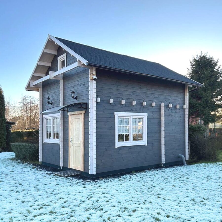 Photo of a small wooden house with gray walls and white trim. Roof with black tiles, two windows on one side, door in the right corner. The house is located on a neat green lawn covered with snow. The house is surrounded by trees and bushes. Natural light. --ar 1:1 --stylize 0 --v 6.1 Job ID: 20db3e56-08ee-43b2-a34f-6b13bc6b7a99