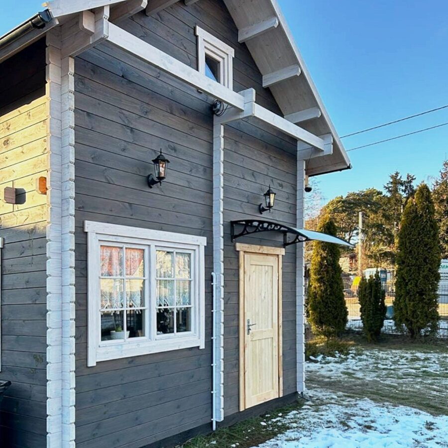 Photo of a small wooden house with gray walls and white trim. Roof with black tiles, two windows on one side, door in the right corner. The house is located on a neat green lawn covered with snow. The house is surrounded by trees and bushes. Natural light. --ar 1:1 --stylize 0 --v 6.1 Job ID: 2632e8bc-575c-4387-bd7b-6b796d06fc61